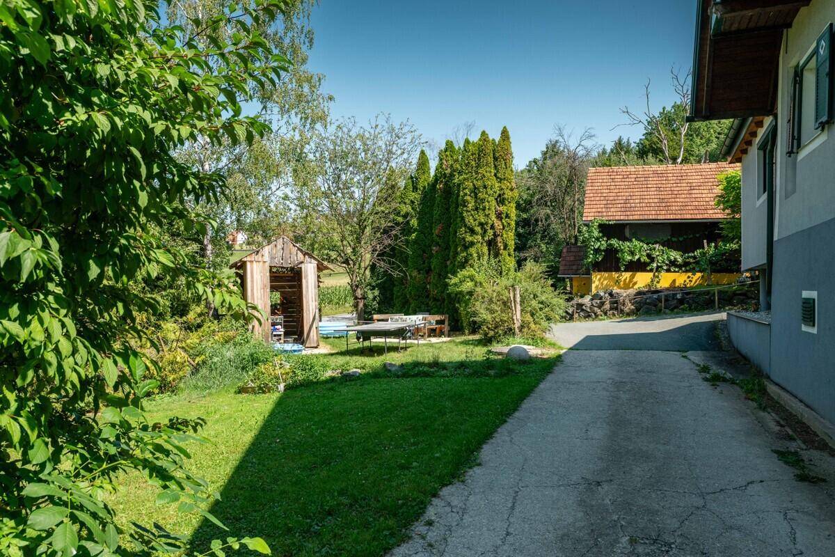 Grüner Gartenweg führt zu einem Gebäude, umgeben von üppiger Vegetation und Bäumen.