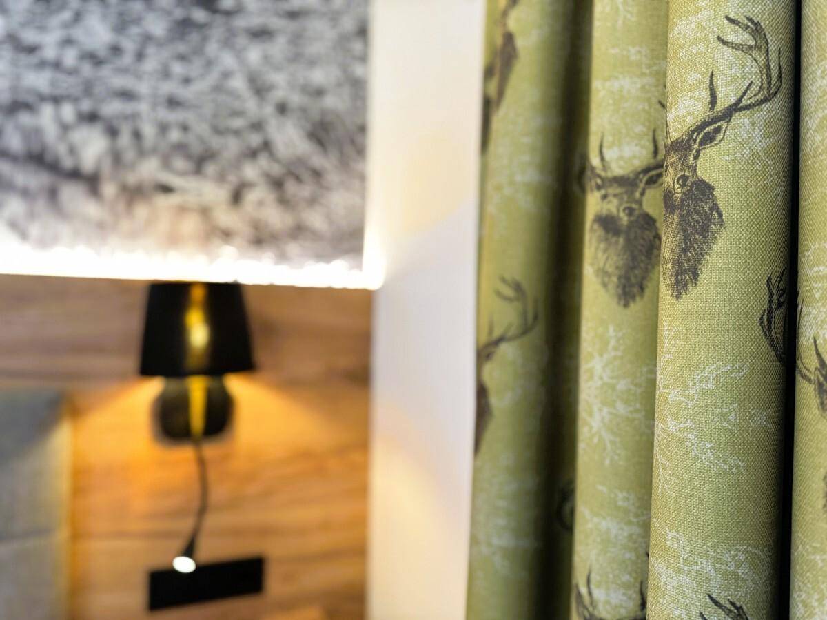 Detailaufnahme des Vorhangs mit Hirschmotiv und der beleuchteten Berglandschaft an der Wand.