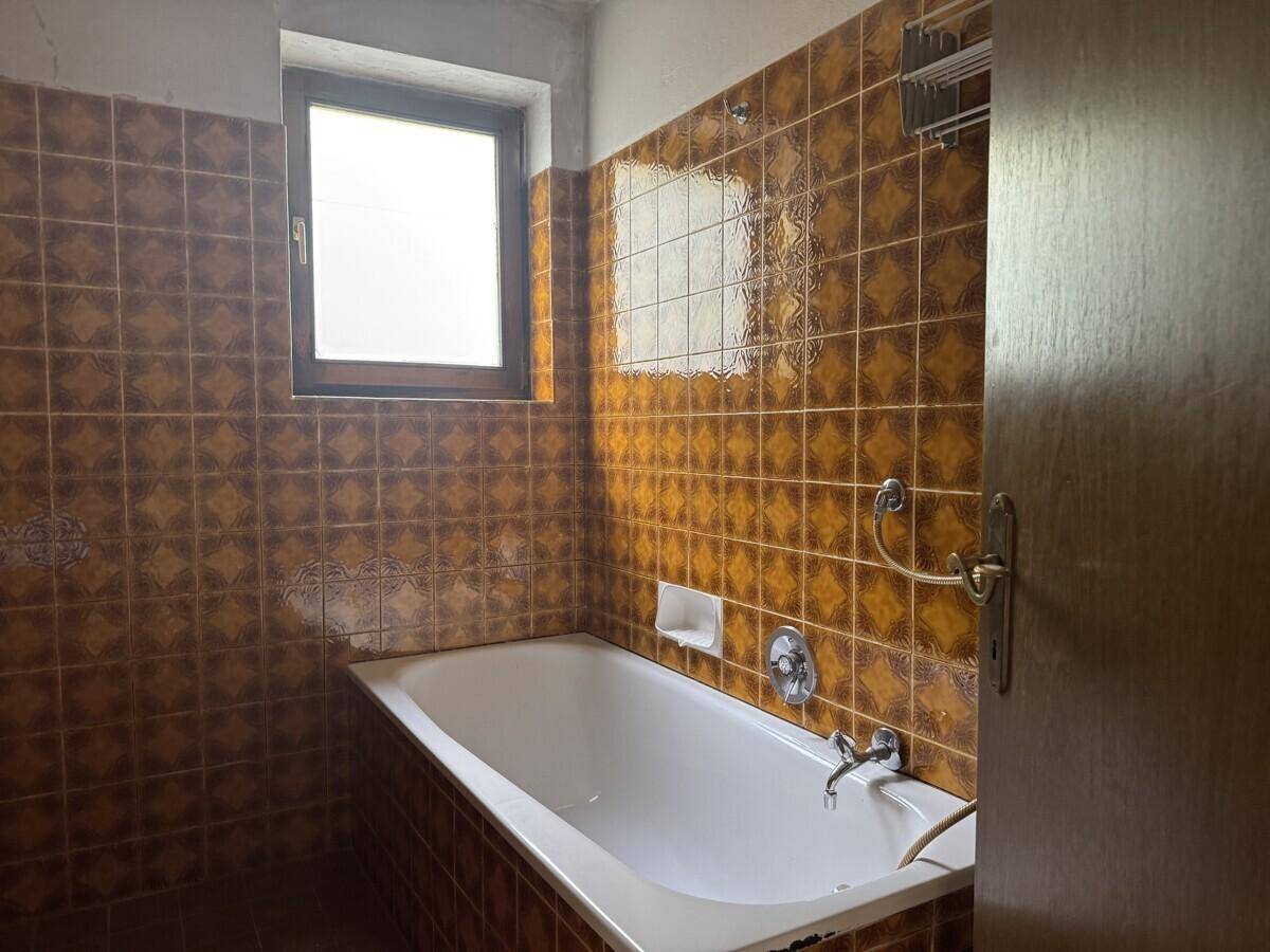 Badezimmer mit braunen Fliesen, Badewanne und Fenster, im Stil der 80er Jahre.