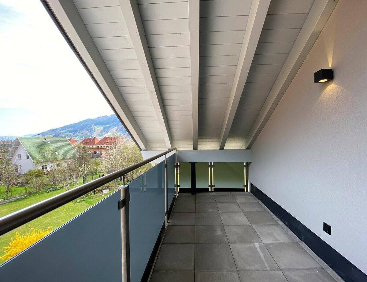 Geräumiger Balkon mit Glasgeländer, Holzdach und weitem Blick auf die Landschaft.