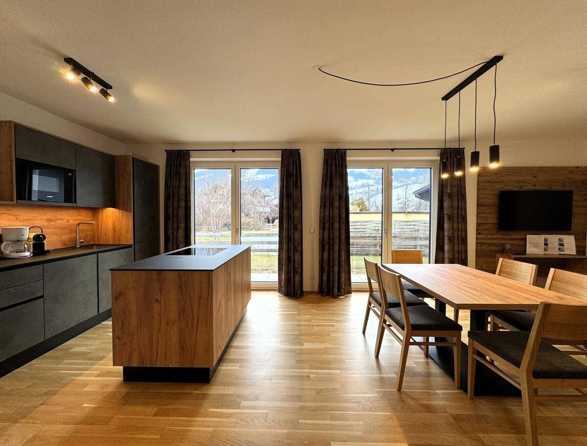 Geräumiger Wohn-Essbereich mit integrierter Küche, Holzboden und großen Fenstern.