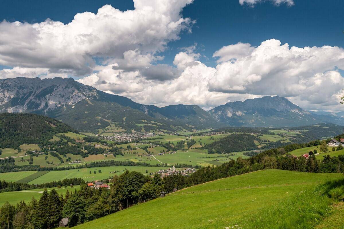 Panoramablick auf eine idyllische Berglandschaft mit weiten grünen Feldern und Dörfern.