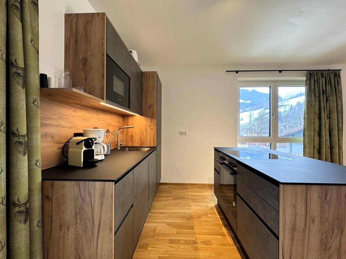 Moderne Küche mit Holz- und Anthrazitfronten, Kochinsel und Fenster mit Bergblick.