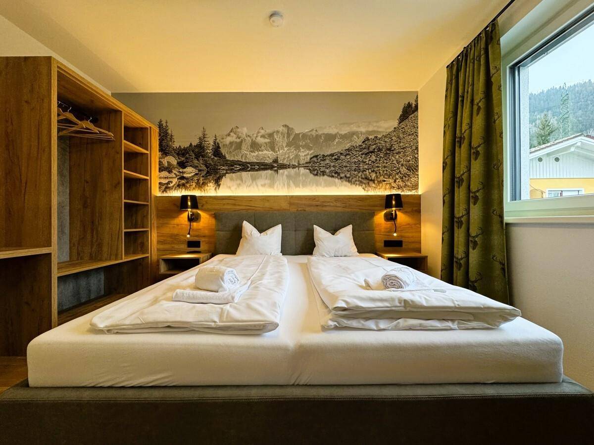 Helles Schlafzimmer mit Doppelbett, Holzelementen und Blick auf die umliegende Landschaft.
