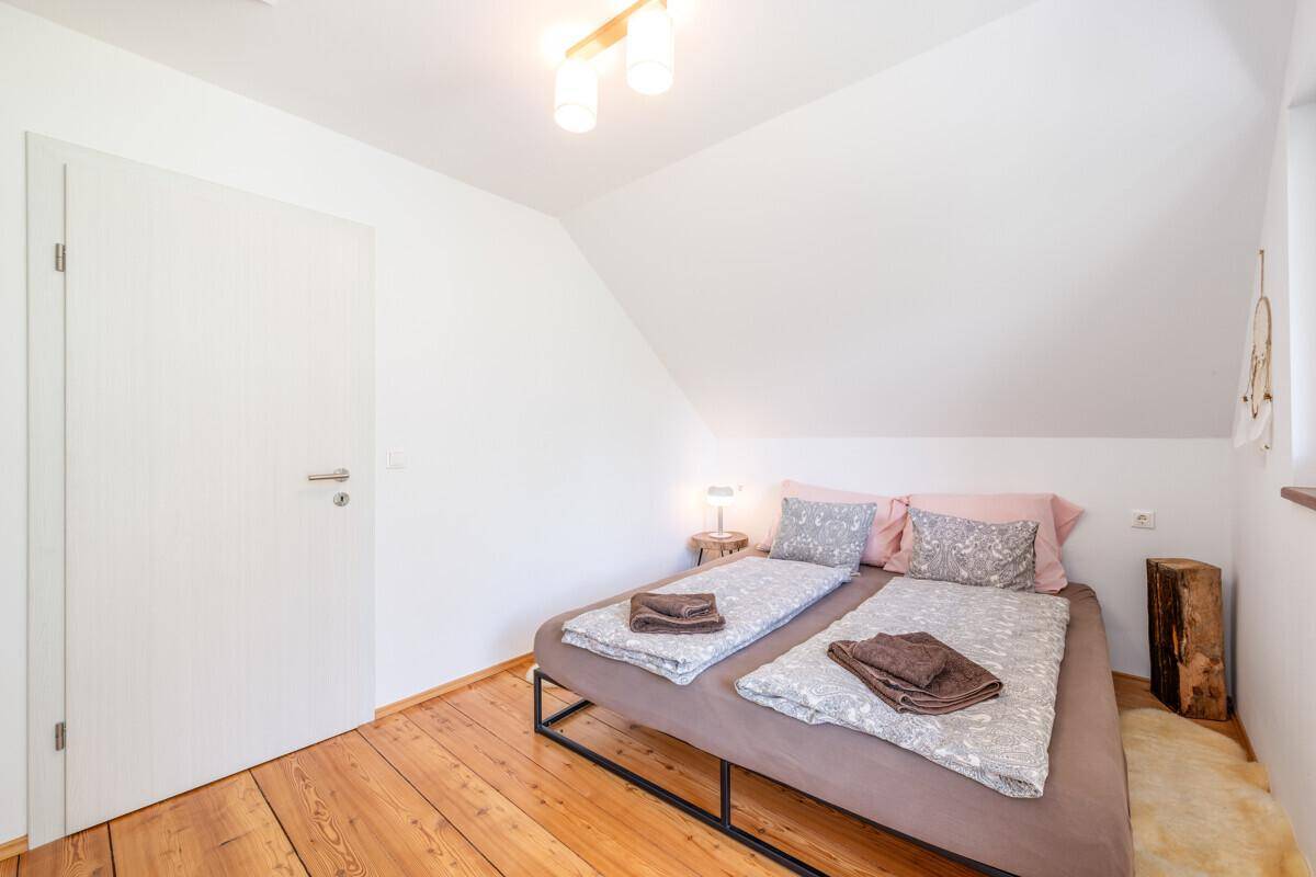 Helles Schlafzimmer mit Doppelbett, Holzboden und schrägen Decken.