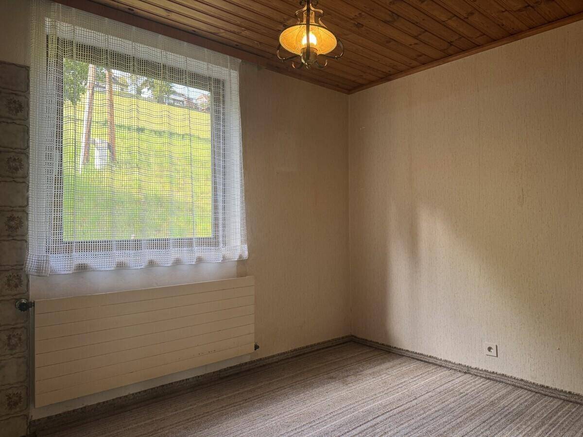 Gemütliches Zimmer mit Teppichboden, Holzdecke und einem Fenster mit Blick ins Grüne.