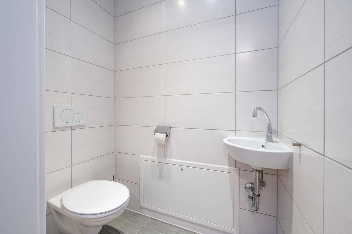 Separate Gästetoilette mit Wand-WC und kleinem Eckwaschbecken, komplett gefliest.