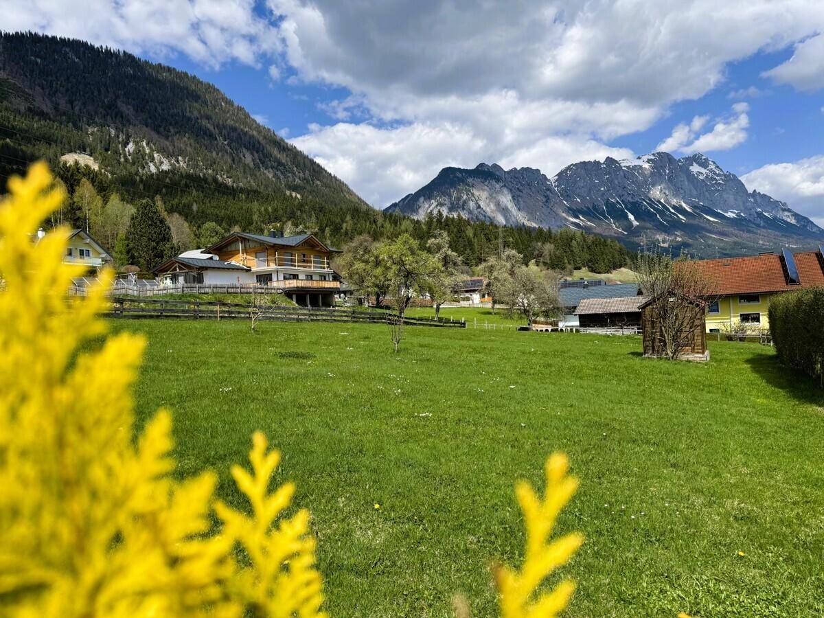 Haus in alpiner Landschaft mit grünen Wiesen und majestätischem Bergblick unter blauem Himmel.