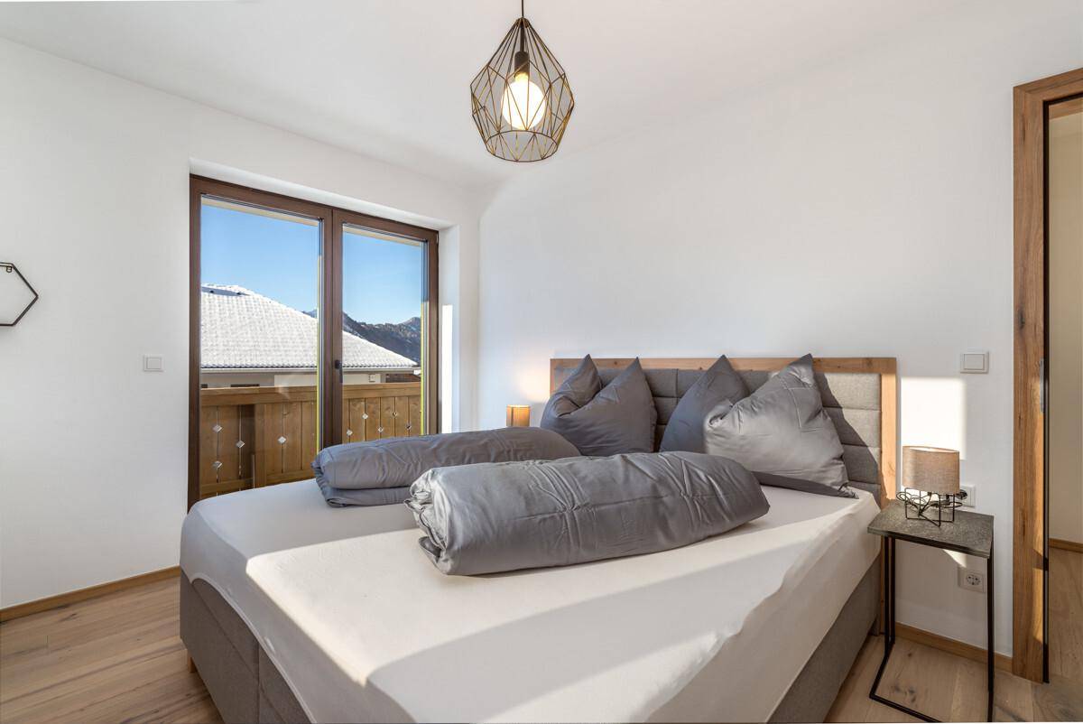 Modernes Schlafzimmer mit Doppelbett, Holzboden und Zugang zum Balkon mit Bergblick.