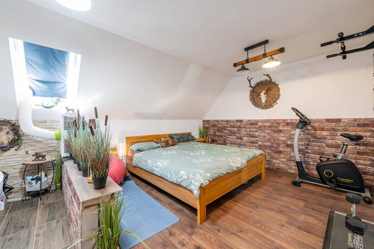 Schlafzimmer mit Holzbett, Heimtrainer und Ziegelstein-Akzentwand unter der Dachschräge.