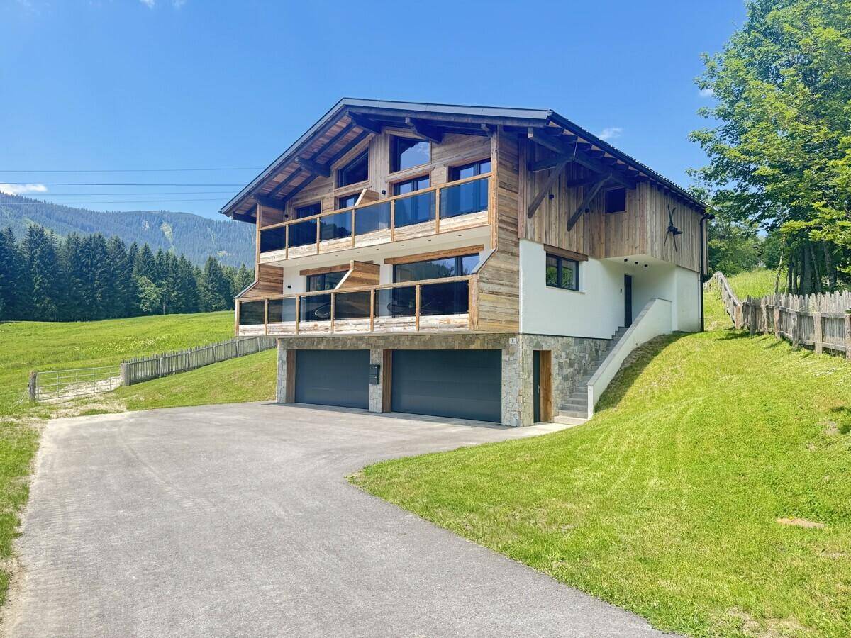 Chaletartiges Gebäude mit Holzfassade, großen Balkonen und Doppelgarage, umgeben von grünen Wiesen.