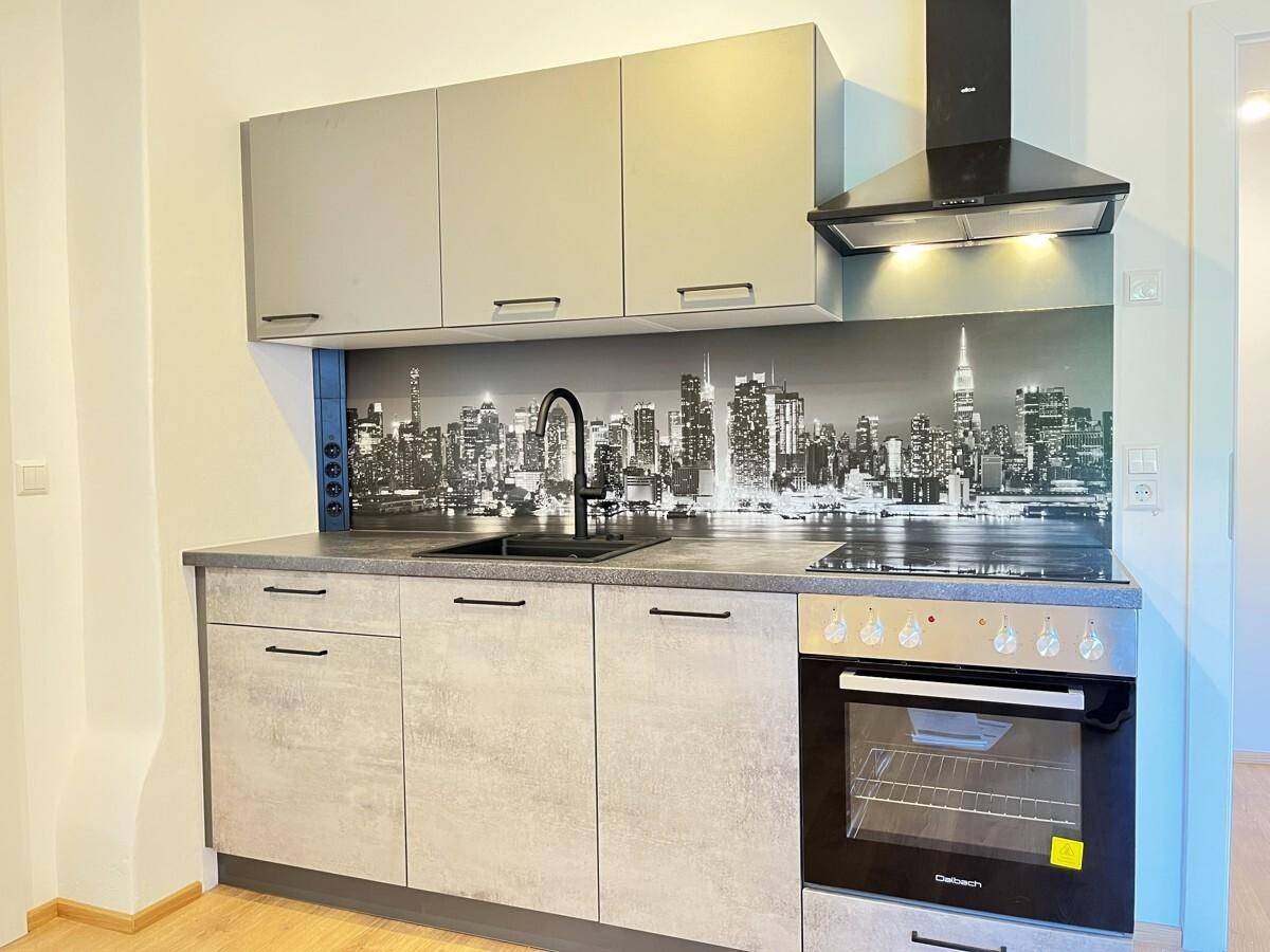 Moderne Küchenzeile mit grauen Schränken, integriertem Backofen und einer stilvollen Skyline-Rückwand.