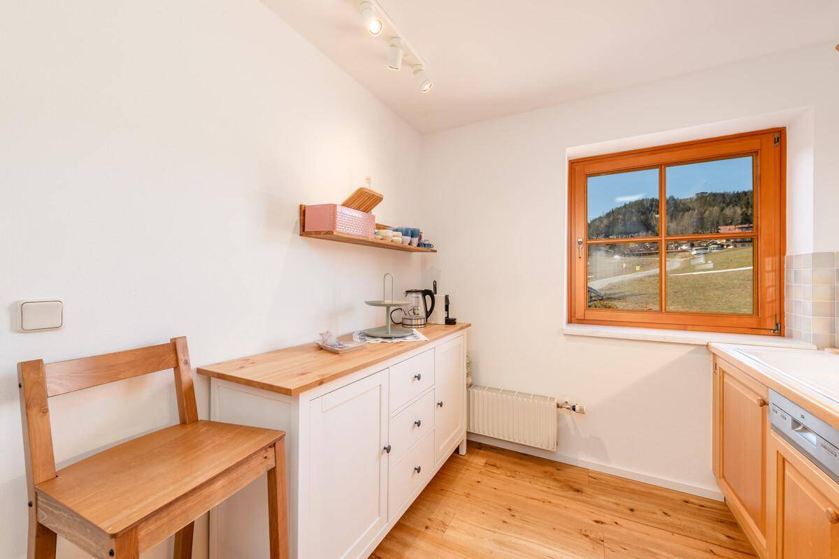 Heller Küchenbereich mit Holzbänken, weißem Schrank und Fenster mit weitem Ausblick.