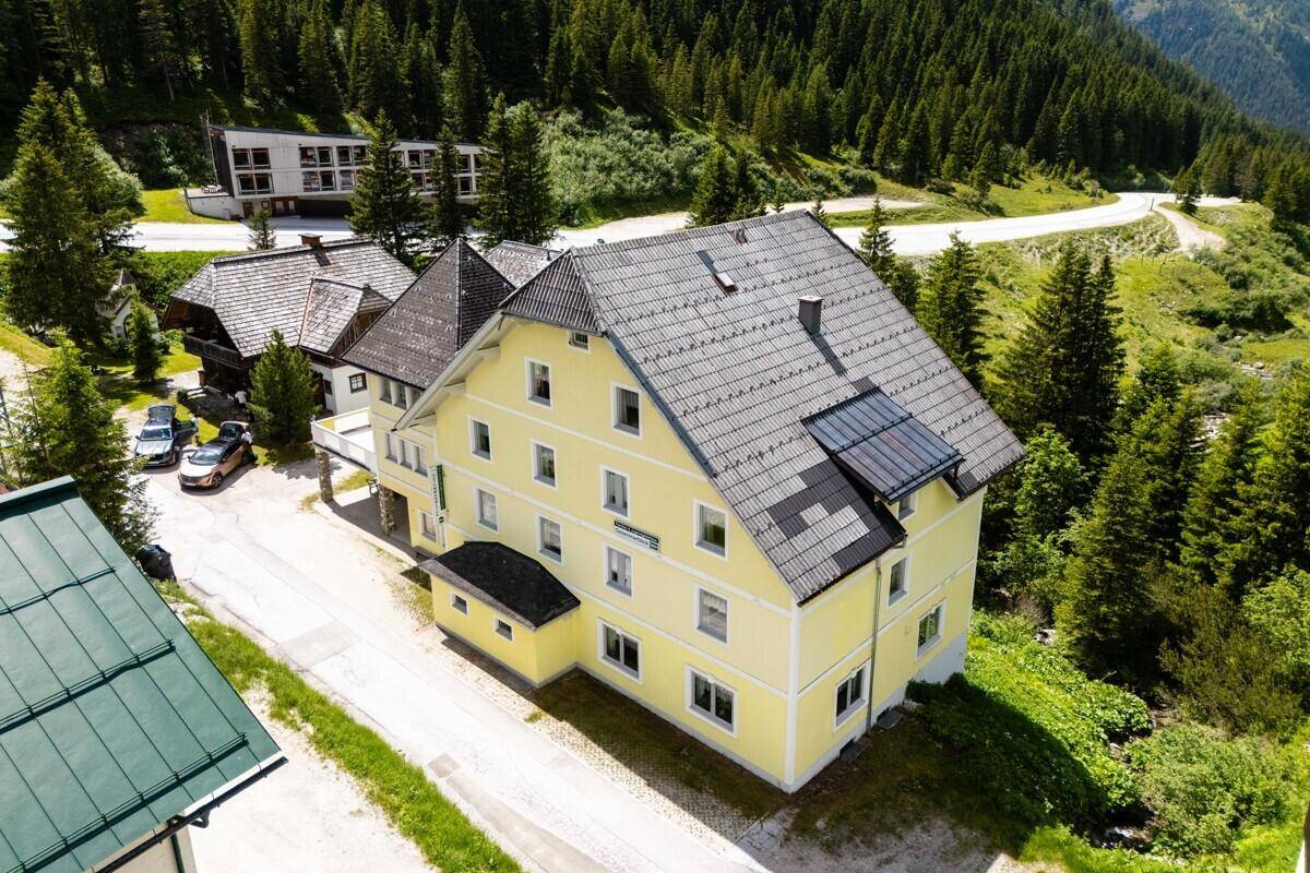Luftaufnahme des gelben Gebäudes mit Solarpaneelen auf dem Dach in einer grünen Bergumgebung.