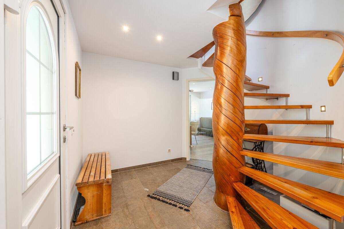 Heller Flur mit eleganter Holzwendeltreppe und modernen Bodenfliesen.