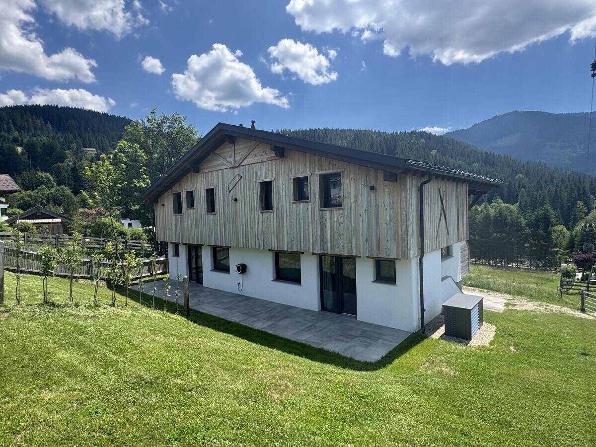 Modernes Chalet mit Holzfassade, großer Terrasse und Photovoltaikanlage in alpiner Umgebung.