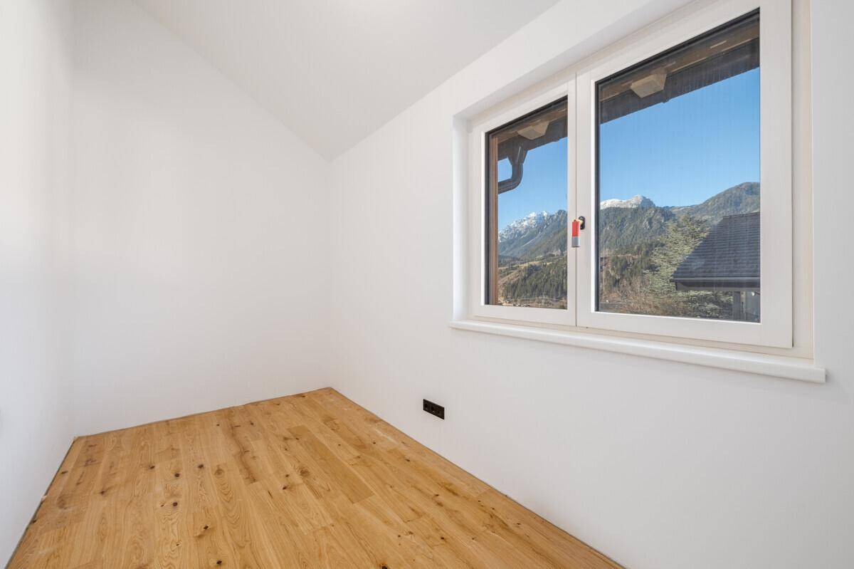 Helles Zimmer mit Holzboden, weißen Wänden und Bergblick durch das Fenster.