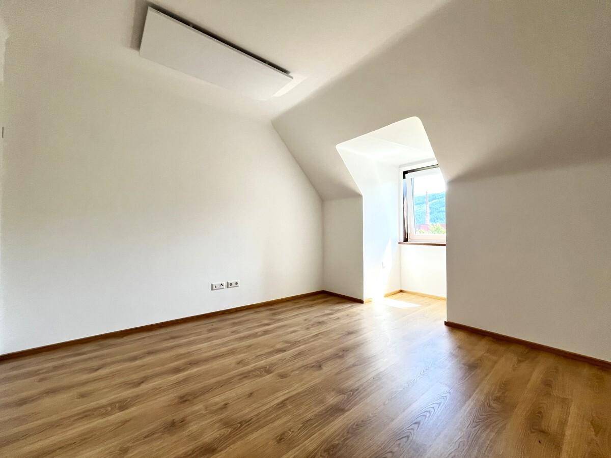 Helles Zimmer mit Laminatboden, weißen Wänden und einem Fenster, das viel Tageslicht hereinlässt.