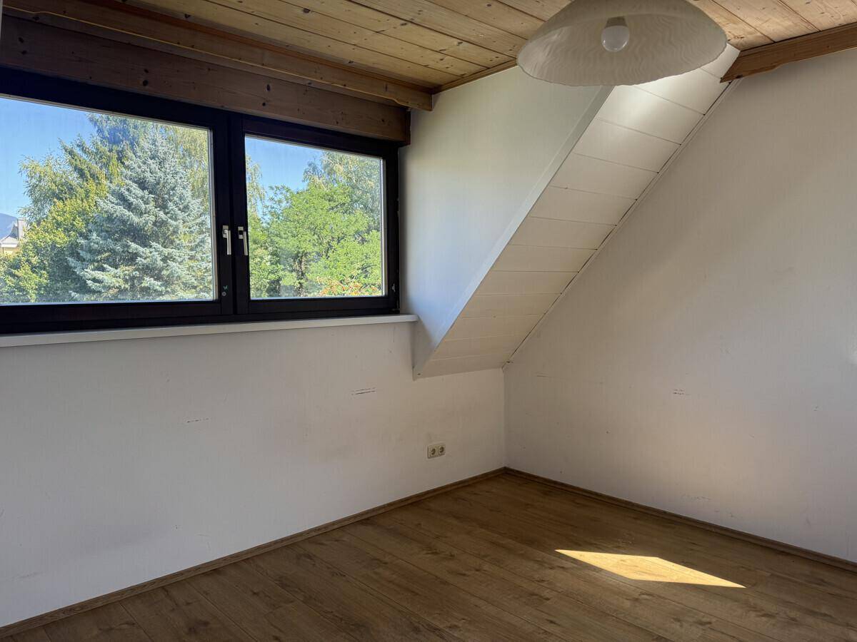 Dachzimmer mit Holzbalkendecke, schrägen Wänden und Blick ins Grüne.