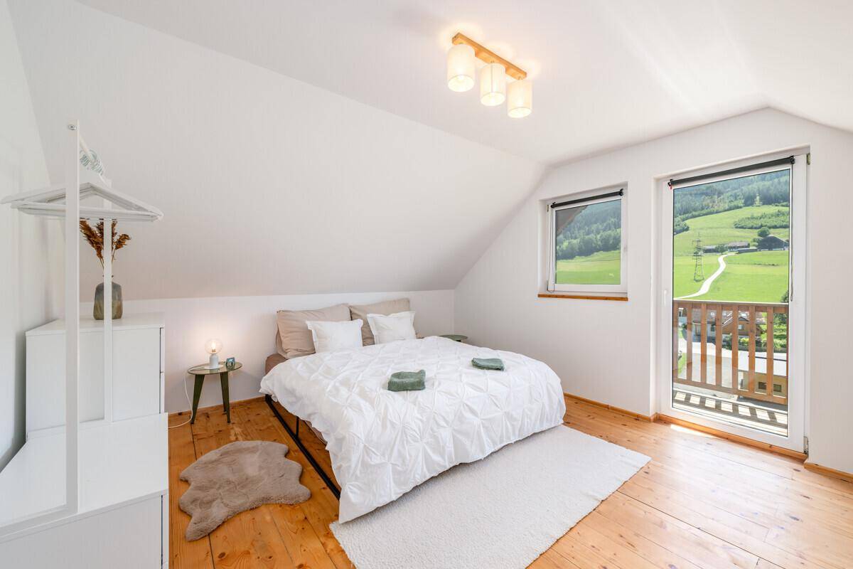 Helles Schlafzimmer im Dachgeschoss mit Holzboden, Balkonzugang und weitem Blick ins Grüne.