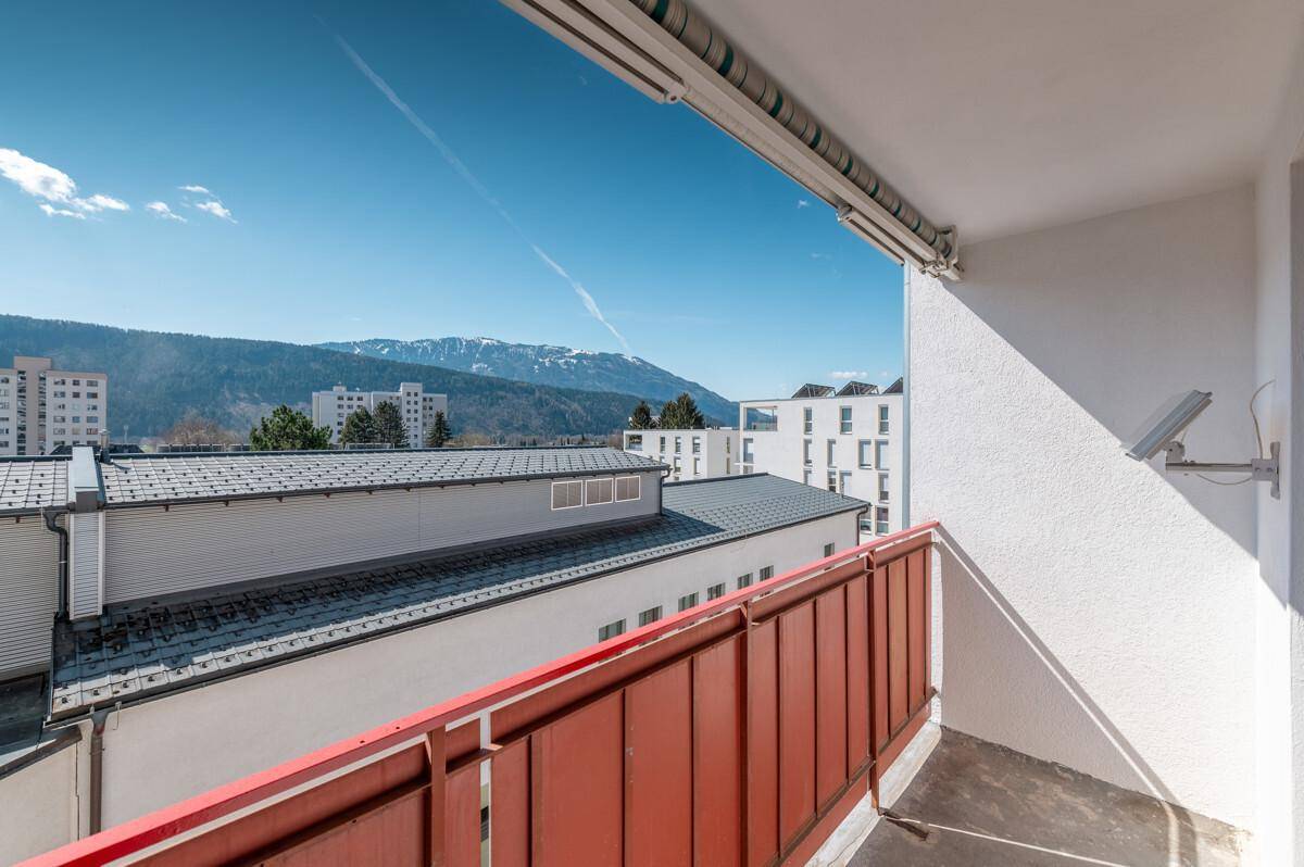 Balkon mit rotem Geländer bietet einen weiten Blick über die Dächer und auf die Berge.