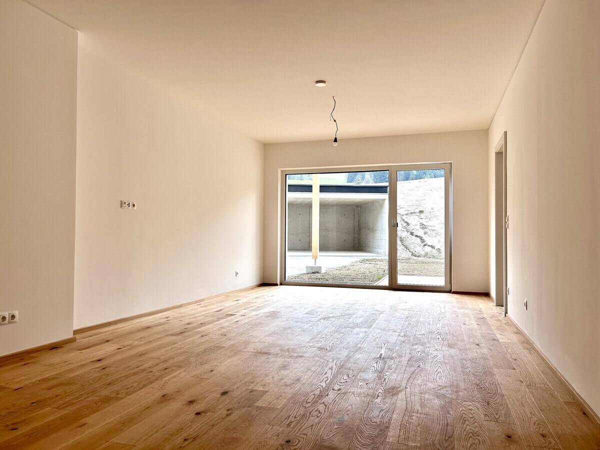 Lichtdurchfluteter Wohnbereich mit Holzboden und großer Schiebetür, die Zugang zum Außenbereich bietet.