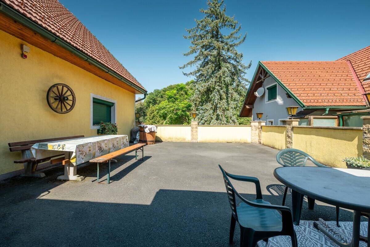 Gepflasterter Außenbereich mit Picknicktisch und Gartenmöbeln, umgeben von Gebäuden und Grün.