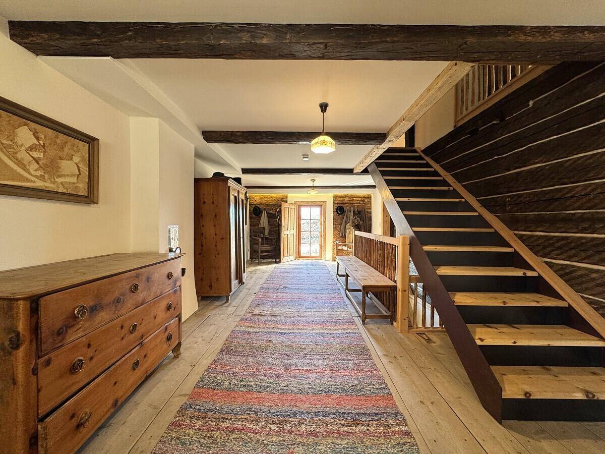 Langer Flur mit Holztreppe, Holzdielenboden und traditionellen Möbeln, die zum Obergeschoss führt.