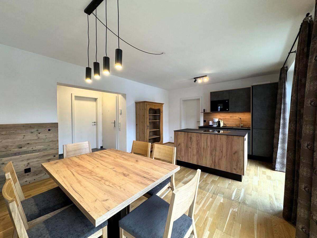 Essbereich mit Holztisch und Stühlen, offener Blick zur Küche und zum Eingangsbereich.
