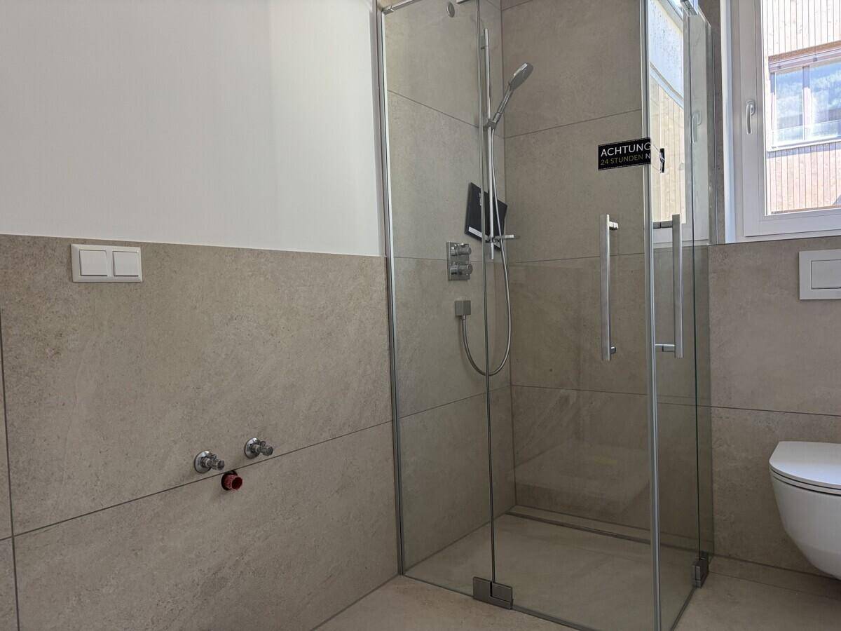 Modernes Badezimmer mit einer Glasdusche, beigefarbenen Fliesen und einem wandhängenden WC.