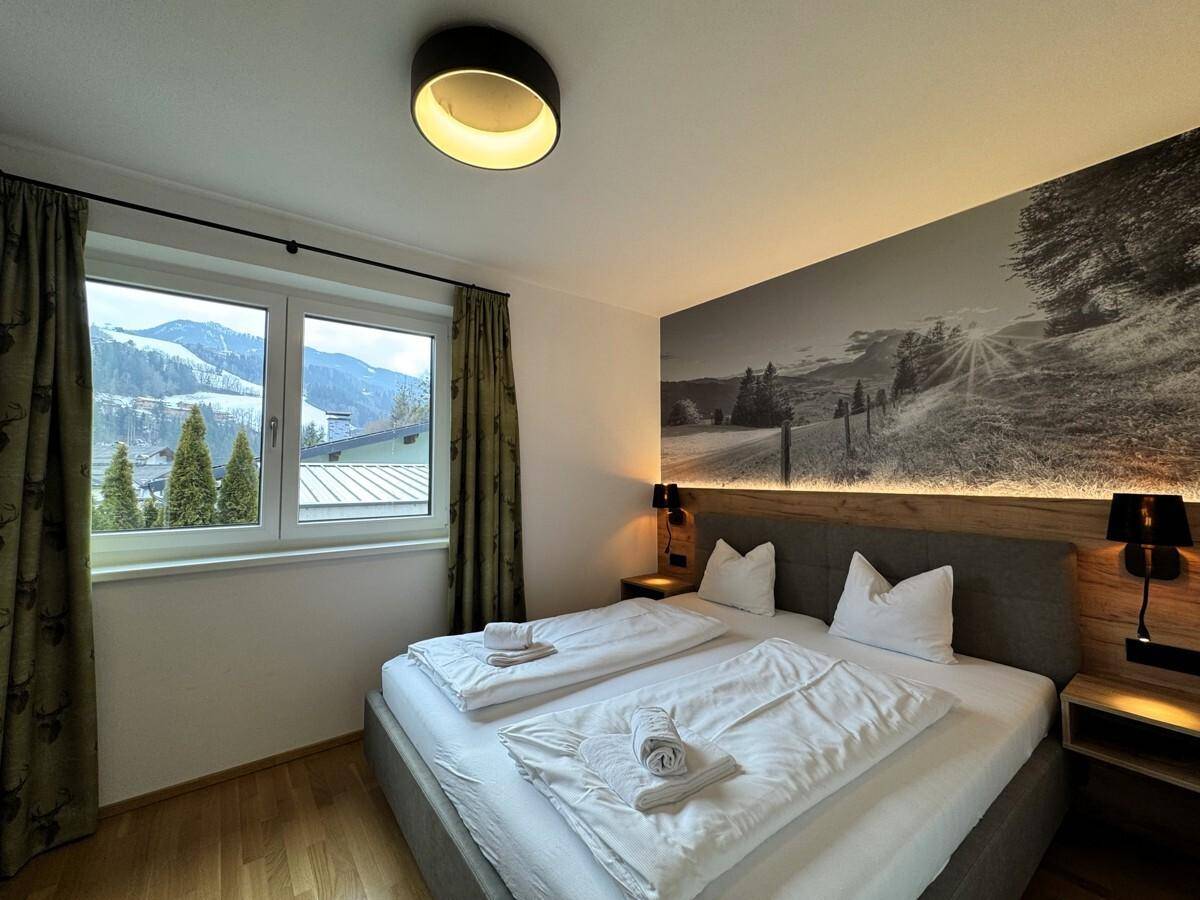 Gemütliches Schlafzimmer mit Doppelbett, Holzboden und Fenster mit Bergblick.