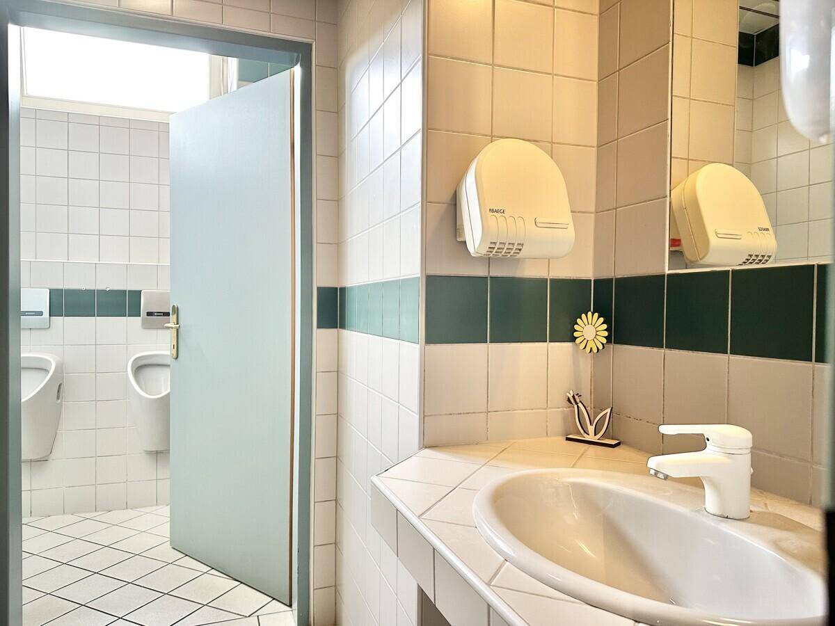 Sauberer Toilettenraum mit weißen und grünen Fliesen, einem Waschbecken und Handtrockner.