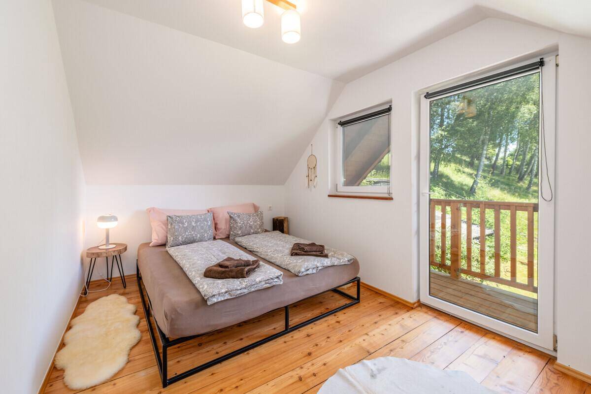 Gemütliches Schlafzimmer mit Doppelbett, Holzboden und Zugang zum Balkon mit grüner Aussicht.