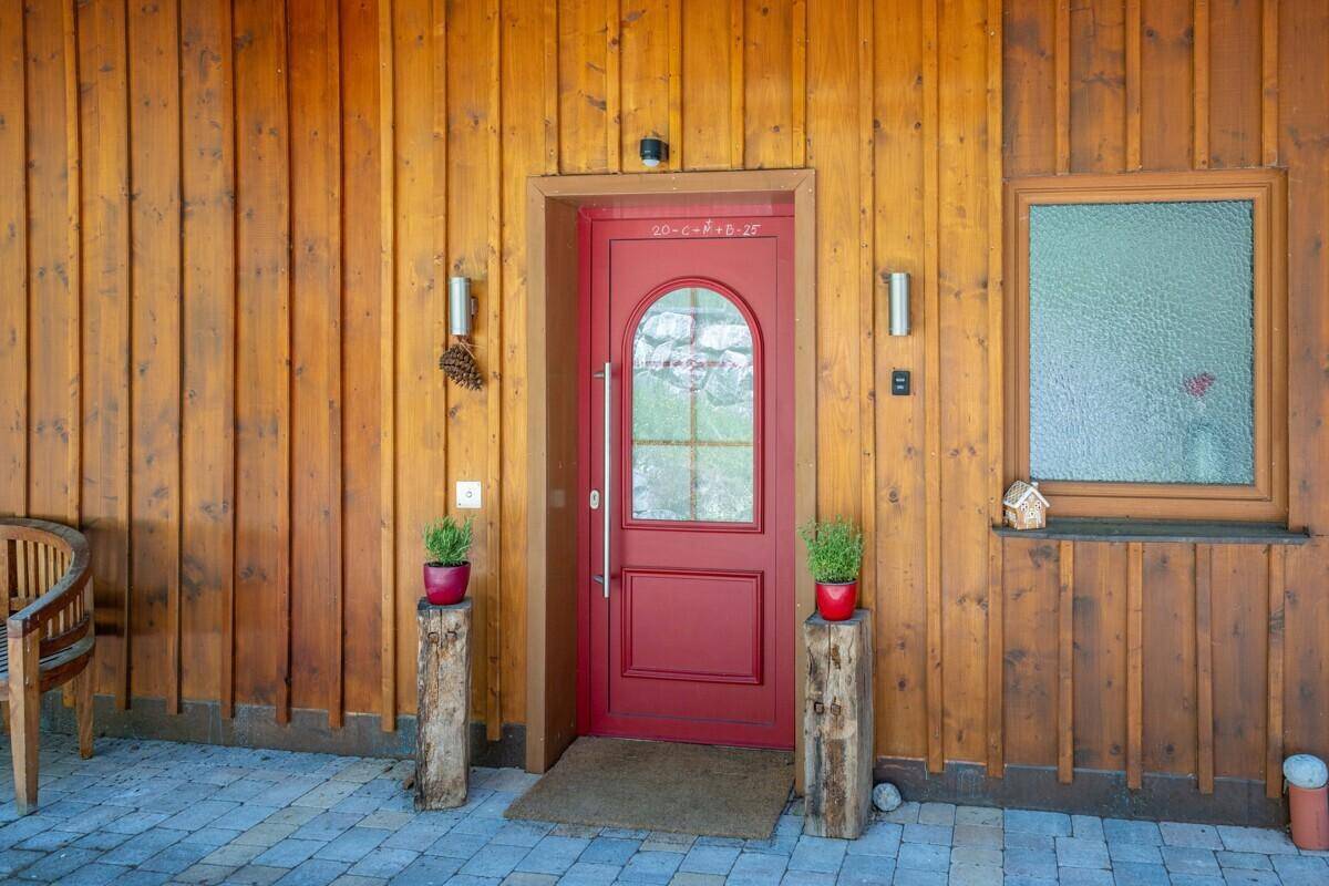 Traditionelle rote Eingangstür mit Holzwänden und gepflastertem Bereich davor.