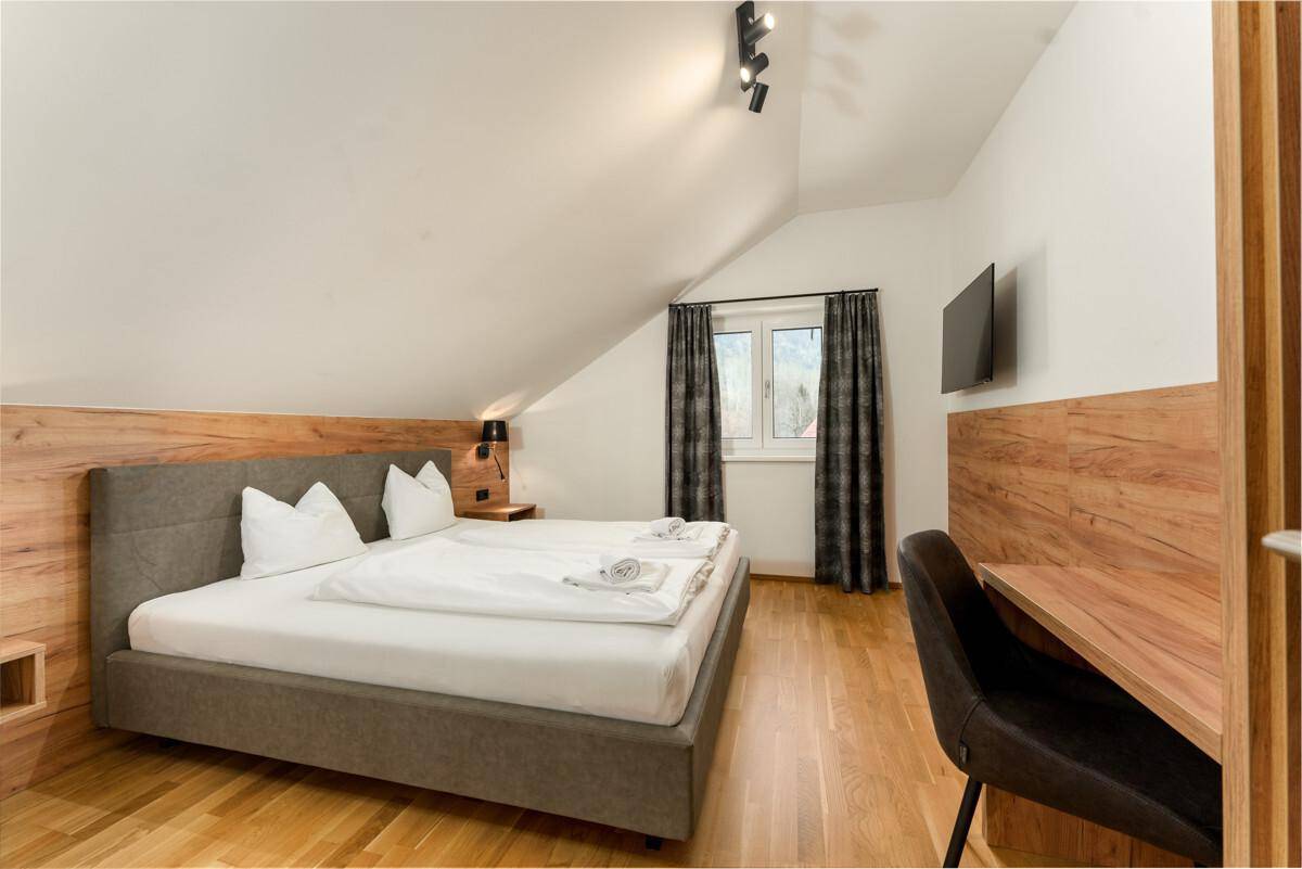 Komfortables Schlafzimmer mit Doppelbett, Holzakzenten und Fenster mit Bergblick.