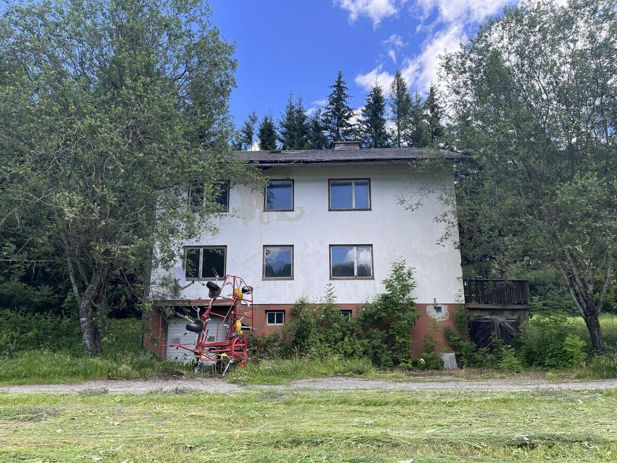 Wohnhaus in ländlicher Umgebung mit Bäumen, grüner Wiese und landwirtschaftlichem Gerät.