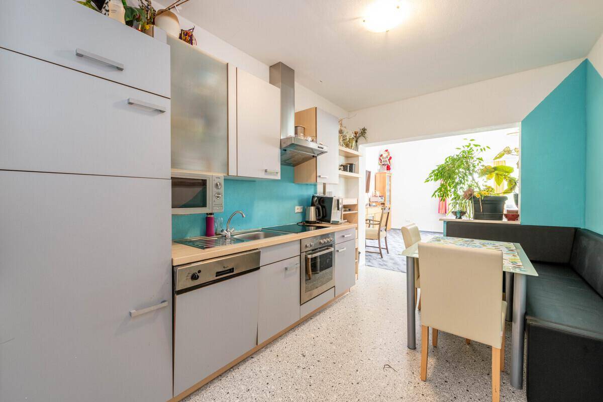 Moderne Küche mit grauen Schränken, blauer Rückwand und einem integrierten Essbereich.