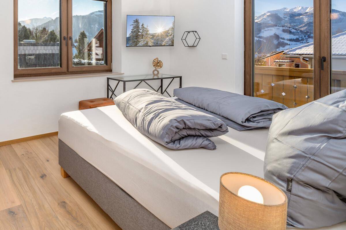 Helles Schlafzimmer mit Doppelbett, Holzboden und großem Fenster mit Bergblick.