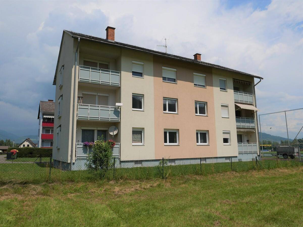 Mehrfamilienhaus mit mehreren Balkonen und gepflegter Grünfläche im Vordergrund.