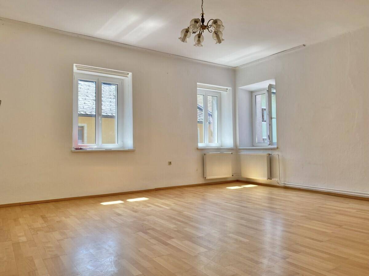 Helles Zimmer mit Fischgrätparkett, weißen Wänden und mehreren Fenstern, bereit zur Einrichtung.