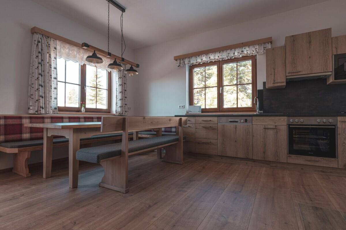 Moderne Wohnküche mit Holzeinbauten, Essbereich und Blick ins Grüne durch große Fenster.