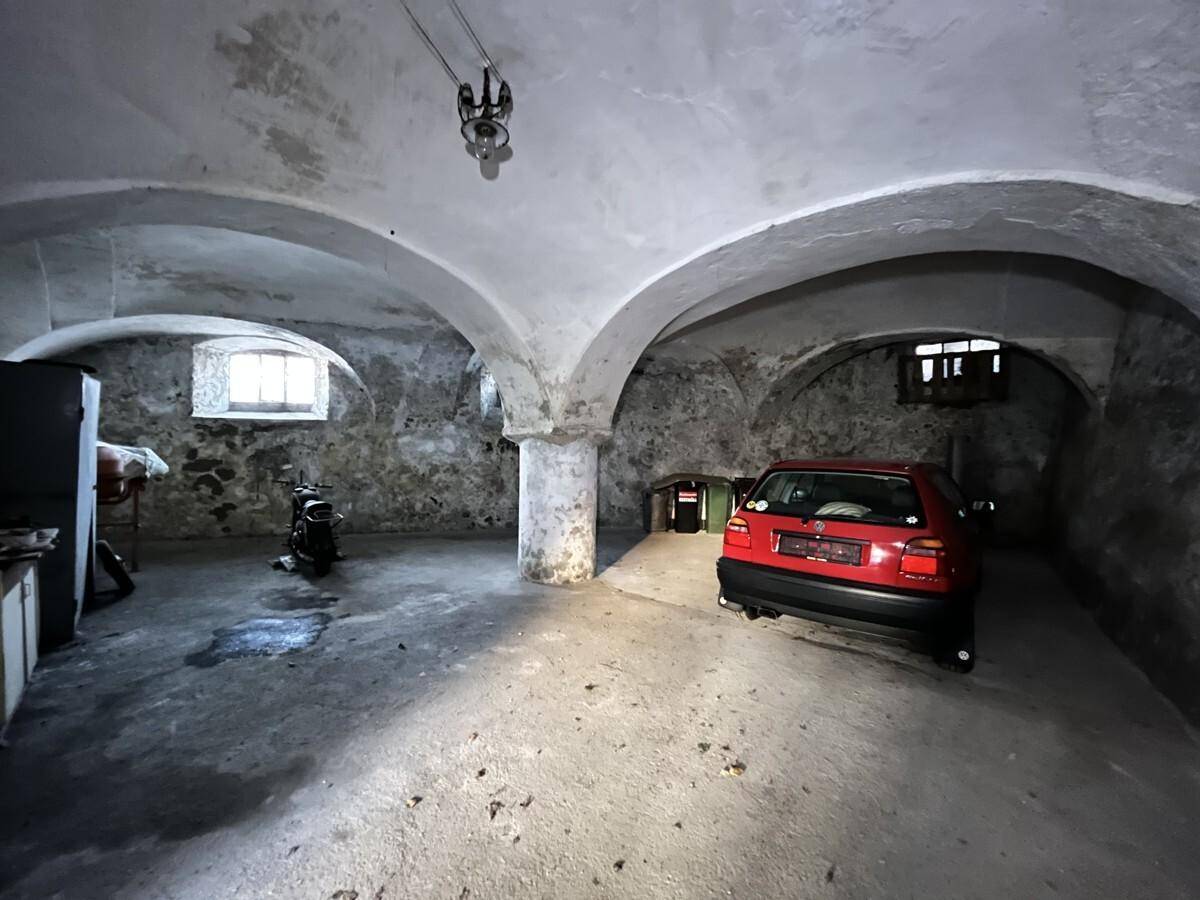 Geräumiger Kellerraum mit Gewölbedecken, kleinen Fenstern und einem geparkten Auto, der Renovierung benötigt.