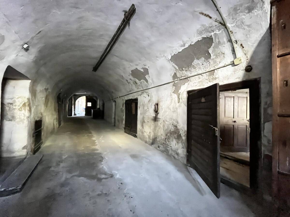 Historischer Gewölbegang mit mehreren Türen und sichtbaren Abnutzungsspuren, der zu weiteren Räumen führt.