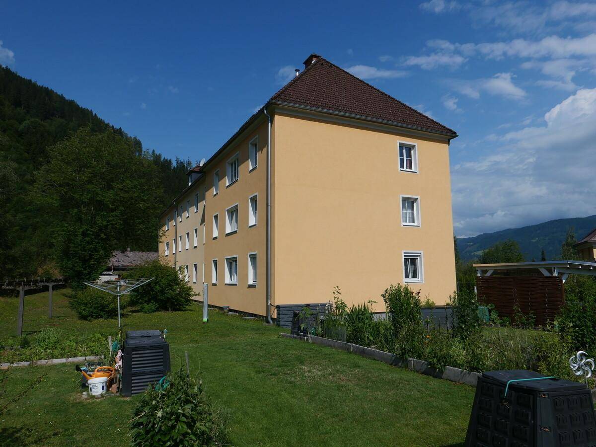 Mehrfamilienhaus mit gepflegtem Gartenbereich und Blick auf die umliegende grüne Landschaft.