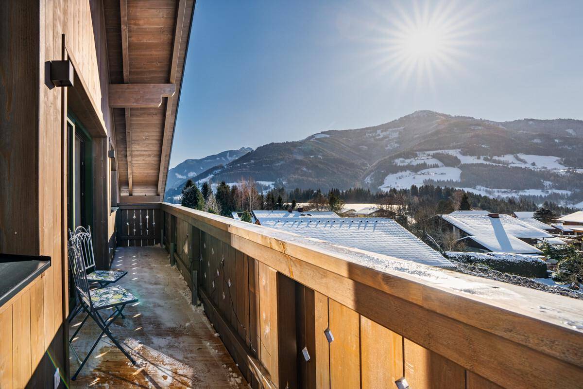 Sonniger Holzbalkon mit Sitzgelegenheiten und beeindruckendem Blick auf die umliegenden Berge.
