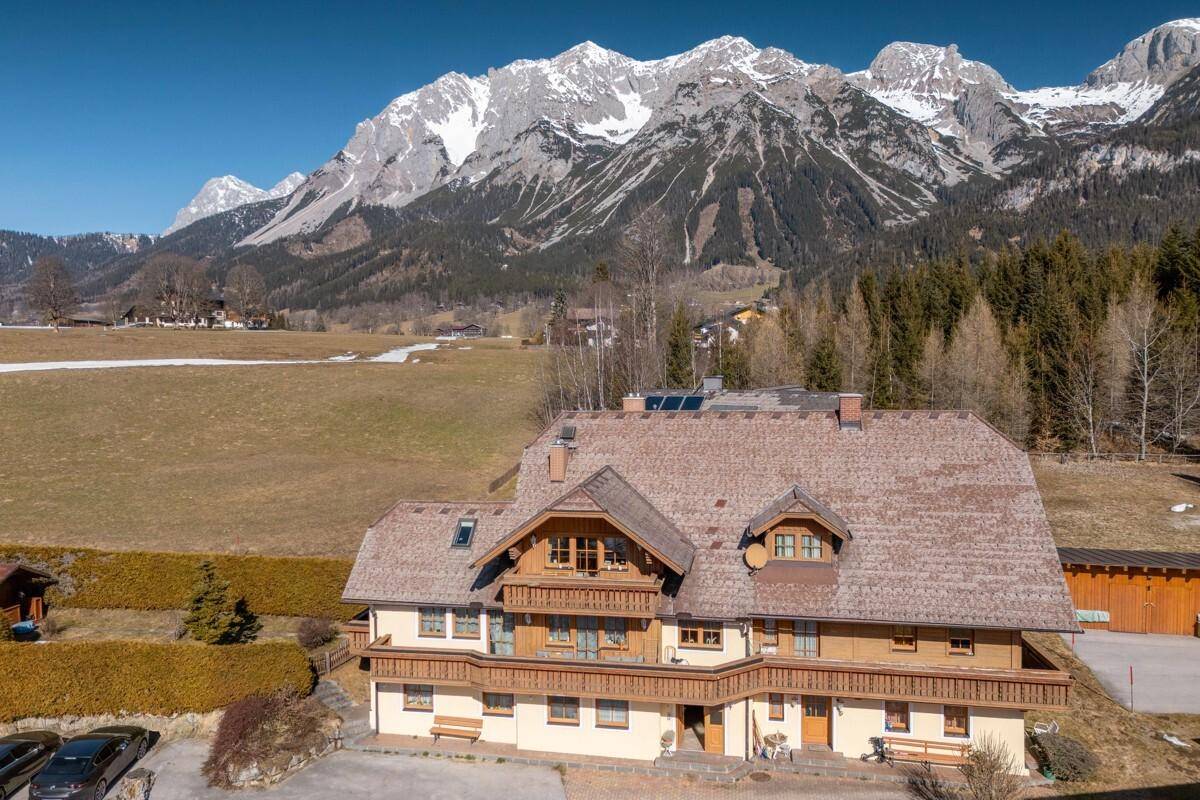 Panoramablick auf ein traditionelles Gebäude in alpiner Umgebung mit schneebedeckten Gipfeln.