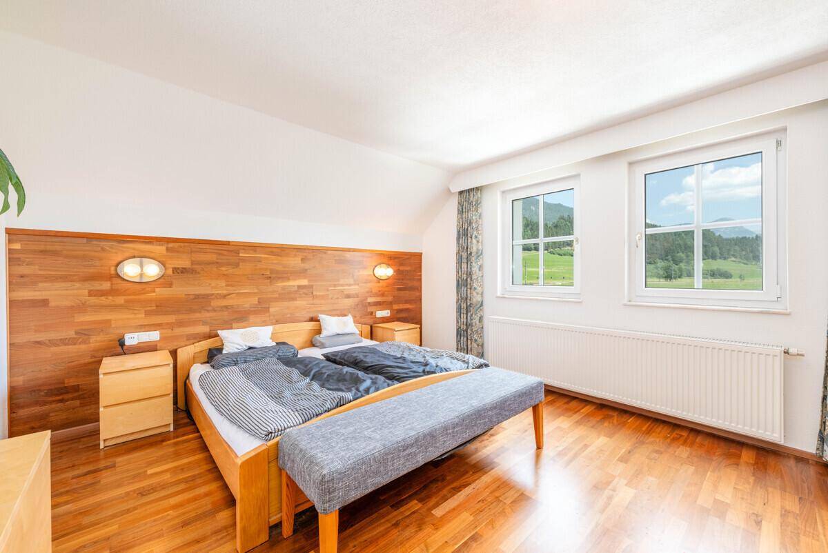 Geräumiges Schlafzimmer mit Holzboden, Doppelbett und Fenstern mit weitem Blick in die Natur.