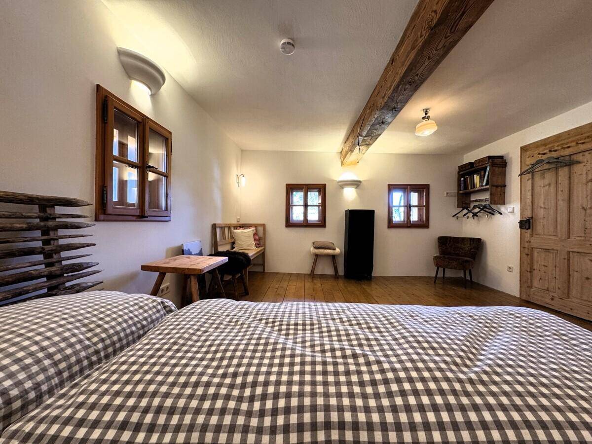 Einfaches Schlafzimmer mit karierter Bettwäsche, Holzdielenboden und kleinen Fenstern, hell und funktional.