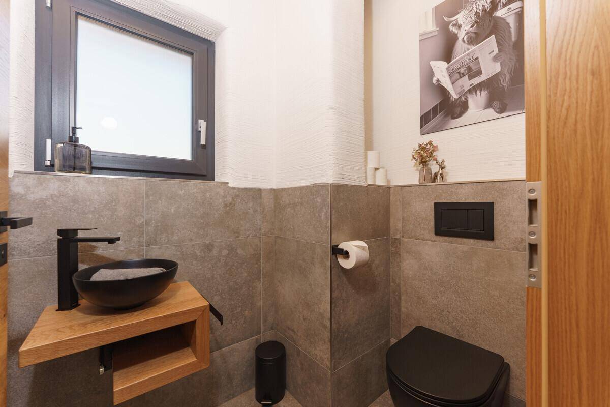 Modernes Gäste-WC mit schwarzer Toilette, Aufsatzwaschbecken und Fenster.