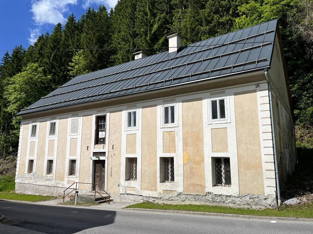 Traditionelles Gebäude mit neuem Dach und Putzfassade, umgeben von grüner Natur.